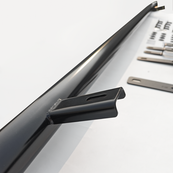 A long black metal bar lays on a white surface, surrounded by several flat metal brackets with hole cutouts, arranged in an orderly fashion.