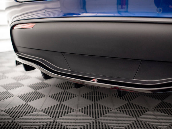 A blue car's rear bumper features a sleek aerodynamic design with a diffuser. A small "ADRO" logo is visible. The car is on a checkered pattern floor, likely in a showroom.