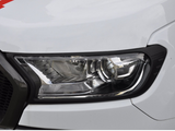 A close-up view of a car headlight, featuring a sleek, angular design with reflective surfaces, set within a white vehicle body. The headlight is bordered by black trim.