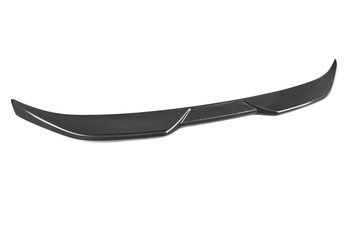 A carbon fiber car spoiler, curved and streamlined, lies against a plain white background, highlighting its smooth, aerodynamic design and textured surface.