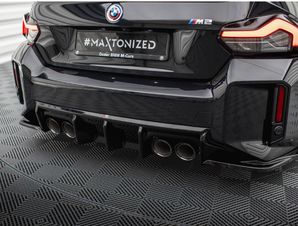 The car's rear features the BMW M2 logo, quad exhausts, and text on the license plate: "#MAXTONIZED Dealer BMW M-Cars," set in a patterned showroom environment.
