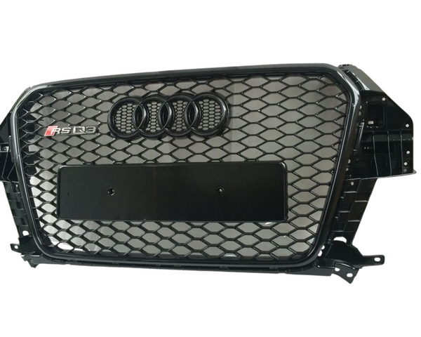 A black car grille with a honeycomb pattern, features four interlocking rings emblem and "RS Q3" text. The grille is designed for an Audi vehicle, displayed against a plain background.