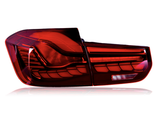 A car taillight is illuminated brightly, featuring a red and intricate design. The taillight is isolated against a plain white background, highlighting its sleek and modern curves.
