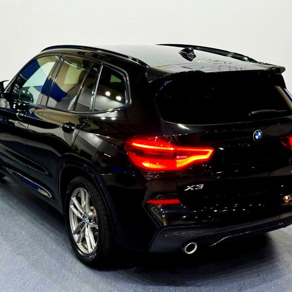 A black SUV with glowing red tail lights is stationary in a showroom, featuring "X3" and "xDrive30d" logos on the rear.