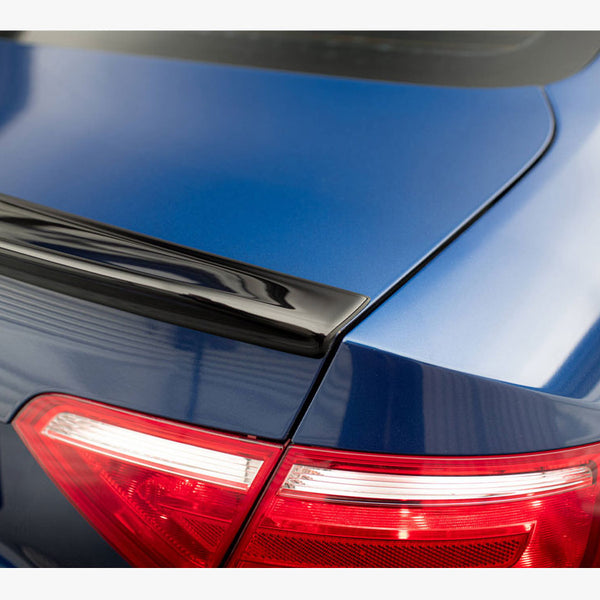 Car rear section features a blue trunk with a black spoiler, and illuminated red tail lights. Partial license plate text reads "ED." The car is parked indoors.