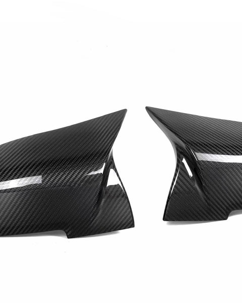 Two black carbon fiber car side mirror covers are positioned against a plain white background, showcasing their glossy, textured surface and sleek, aerodynamic shape.