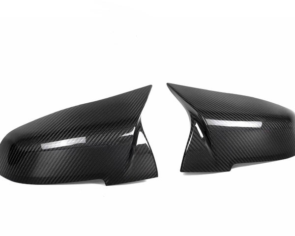 Two sleek carbon fiber side mirror covers are positioned facing each other against a plain white background. The glossy texture highlights their aerodynamic design.