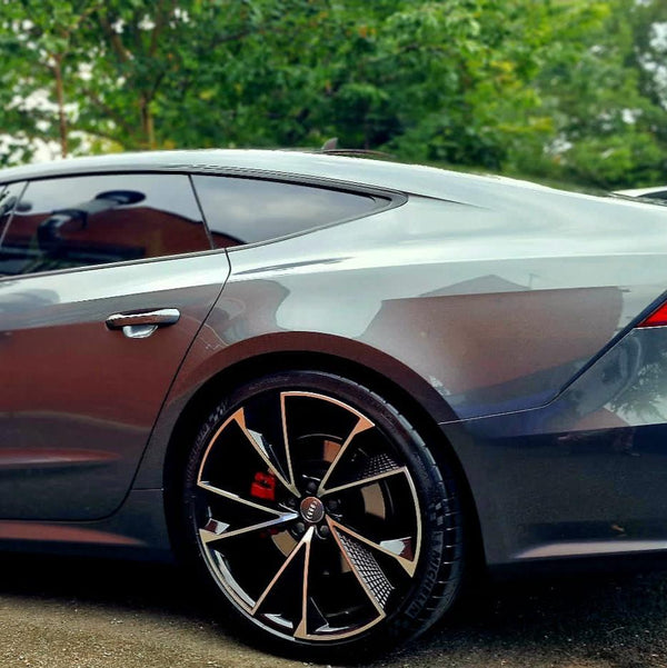 A sleek silver car is parked, showcasing its modern wheel design and smooth body curves. Trees and greenery create a natural backdrop.