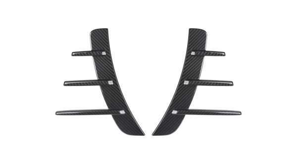 Two black carbon fiber pieces with three horizontal fins each are symmetrically aligned. They are set against a plain white background, suggesting automotive parts.