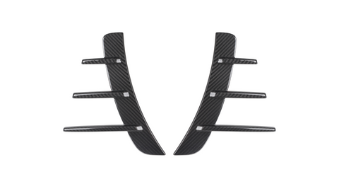 Two black carbon fiber pieces with three horizontal fins each are symmetrically aligned. They are set against a plain white background, suggesting automotive parts.
