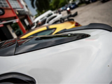 White car with a black roof detail, parked on a street alongside a yellow car. Background includes storefronts and additional parked vehicles.