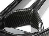 Carbon fiber panel with a glossy finish, featuring intricate weaving patterns, lies on a flat surface. It appears structured and rigid, likely part of an automotive or industrial component.