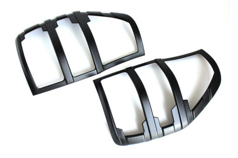 Black plastic tail light covers are lying side by side on a plain white background. They have curved, segmented designs to fit over vehicle tail lights, providing a protective and decorative function.