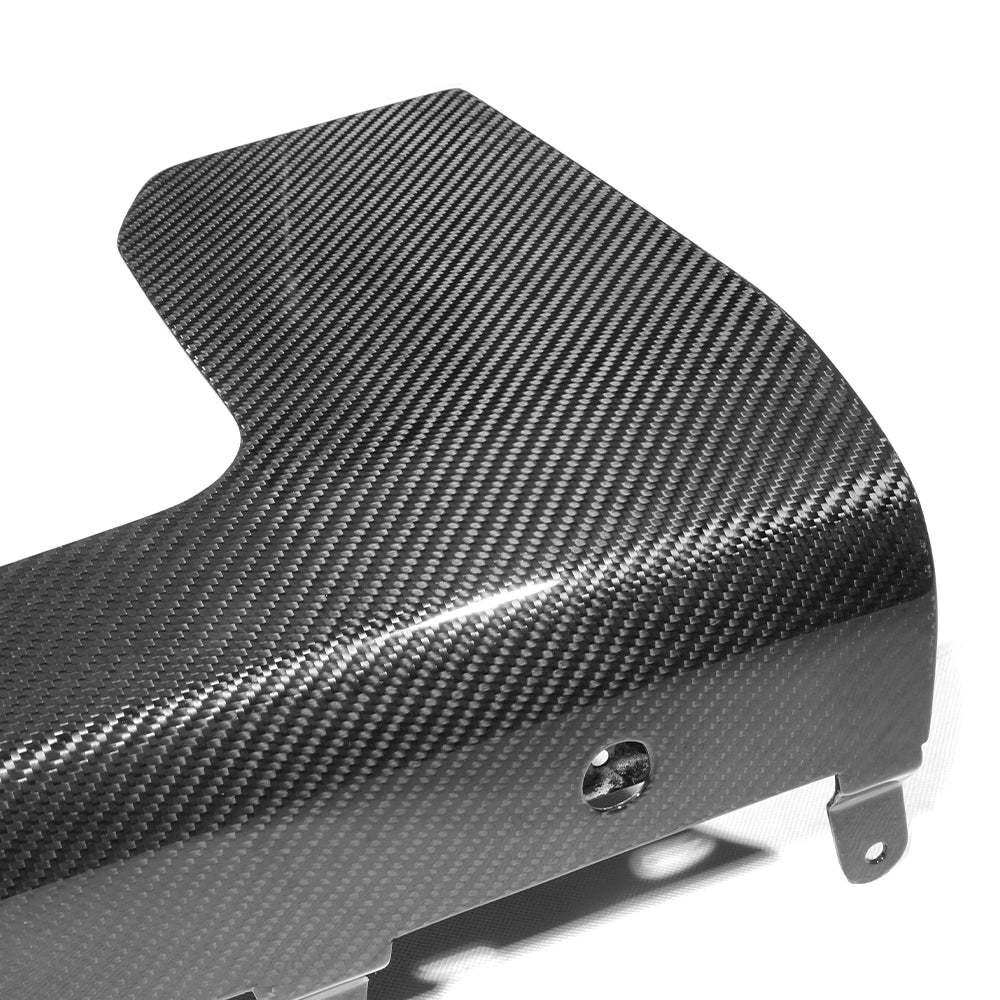 A smooth, angled carbon fiber panel with a diagonal weave pattern lies on a plain white surface, featuring mounting holes and metal brackets along the edges.