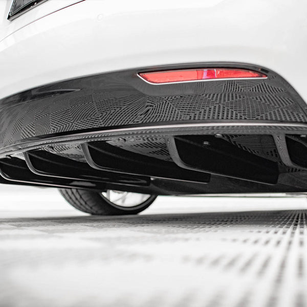 The lower rear section of a white car displays a patterned black diffuser, situated in a well-lit, indoor space with a checkered floor.