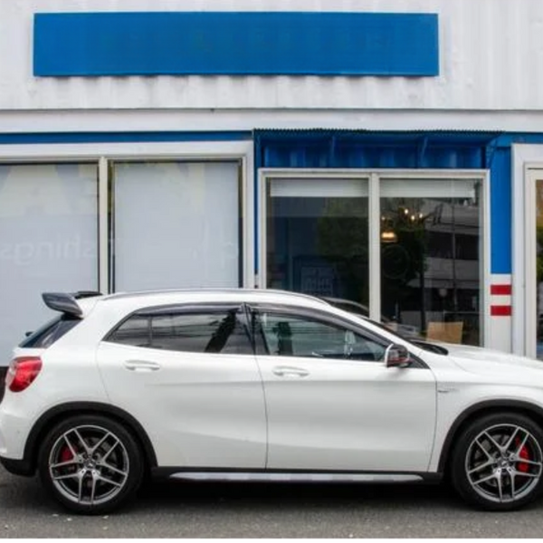 White car parked side view, in front of a building with glass doors and a blue and red striped facade. The car is stationary, and the setting is urban. No visible text.