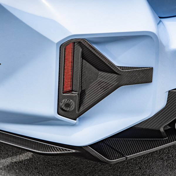 A light blue car's rear, featuring a carbon fiber diffuser and red taillight, with dual exhaust pipes and visible tire tread, on a textured road surface.