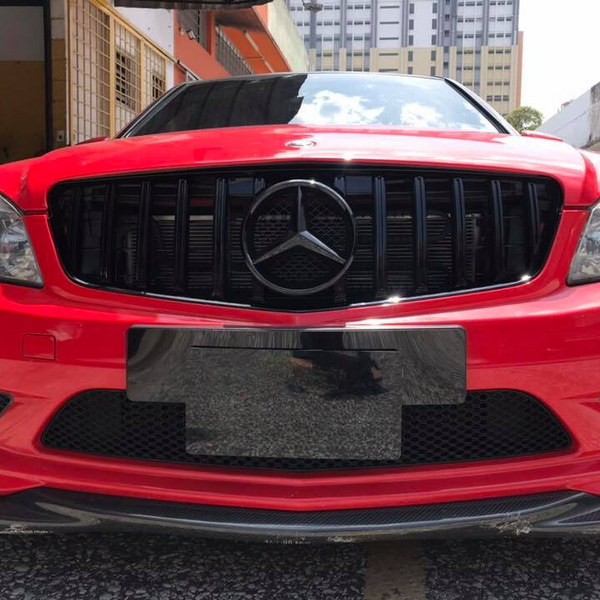 A red Mercedes-Benz car is parked in an urban environment, displaying a black grille with a prominent Mercedes emblem and surrounded by buildings.