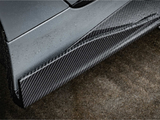 A sleek car's carbon fiber side skirt, covered in raindrops, sits adjacent to a wet asphalt surface, highlighting the vehicle's modern design and performance-oriented components.