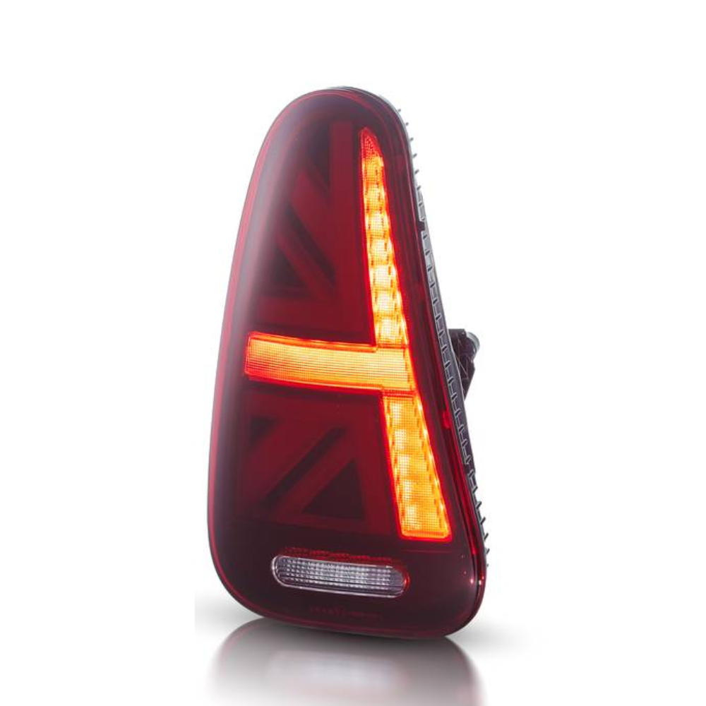 A triangular taillight displays a bright red and amber pattern reminiscent of the Union Jack. It is illuminated against a plain white background, highlighting its design.