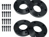 Four black wheel spacers with circular holes are laid out on a white surface, accompanied by sixteen matching screws arranged in two vertical rows.