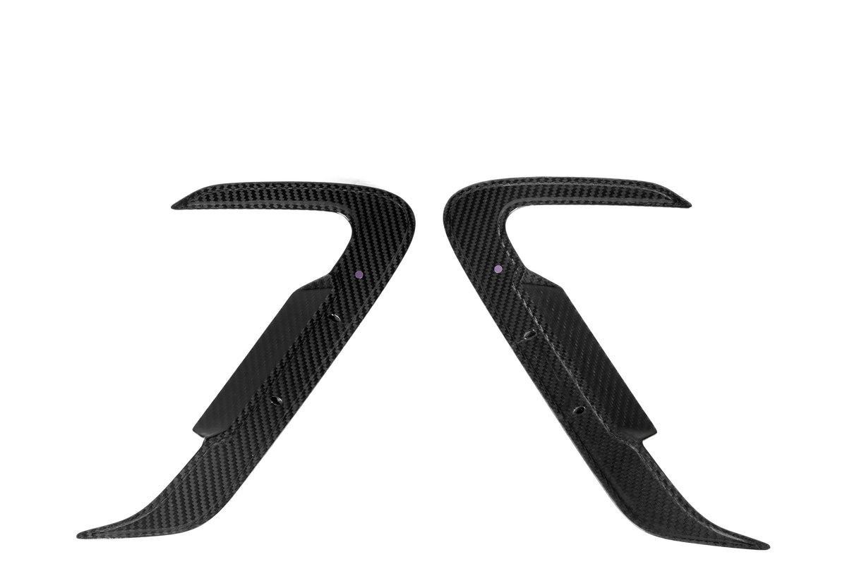 Two curved, black carbon fiber car parts with pointed ends face each other symmetrically on a plain white background, displaying polished surfaces and small holes near the center.