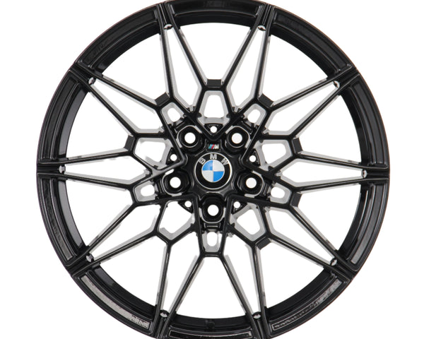 A black, intricately designed alloy wheel rim with the BMW logo at its center, viewed directly from the front, set against a plain white background.