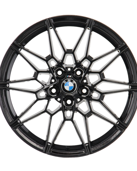 A black, intricately designed alloy wheel rim with the BMW logo at its center, viewed directly from the front, set against a plain white background.