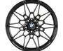 A black, intricately designed alloy wheel rim with the BMW logo at its center, viewed directly from the front, set against a plain white background.