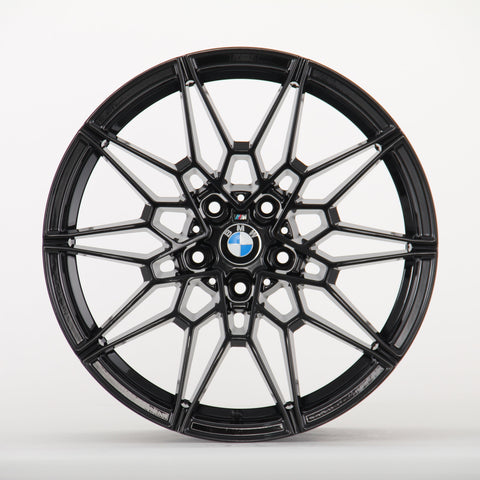 A black, multi-spoke alloy wheel displays a BMW logo at the center, set against a plain white background, highlighting its intricate design.