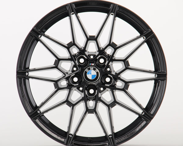 Black, intricately designed alloy wheel with a BMW logo in the center; it rests against a plain white background.
