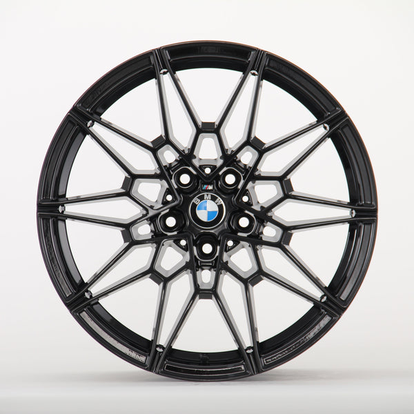 A black, intricately designed car wheel rim with a central BMW logo is displayed against a plain white background, showcasing its geometric pattern and sleek finish.