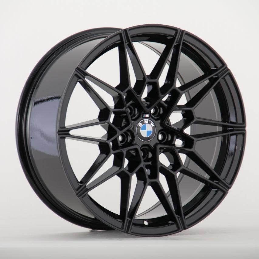 A glossy black alloy wheel with intricate geometric spokes features a centered BMW logo. It is positioned against a plain white background.