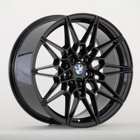 A glossy black alloy wheel with intricate geometric spokes features a centered BMW logo. It is positioned against a plain white background.