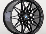 A black alloy wheel with a geometric, multi-spoke design rests upright against a plain white background. The center features the BMW logo, displaying an aesthetic blend of elegance and functionality.