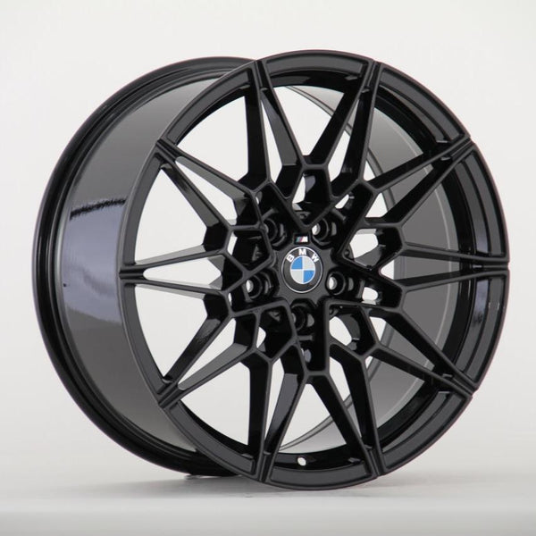 A black alloy wheel with a geometric, multi-spoke design rests upright against a plain white background. The center features the BMW logo, displaying an aesthetic blend of elegance and functionality.