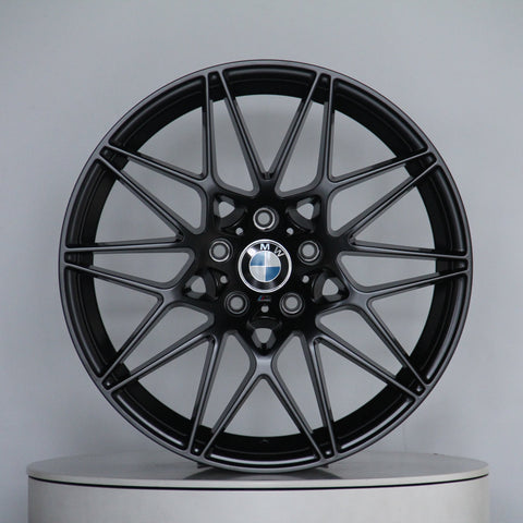 A sleek black alloy wheel with a multi-spoke design, featuring the BMW logo at its center, stands on a plain circular platform in a light gray setting.