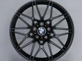 A black alloy wheel with multi-spoke design, featuring a central BMW logo, rests on a round display platform against a plain gray background.