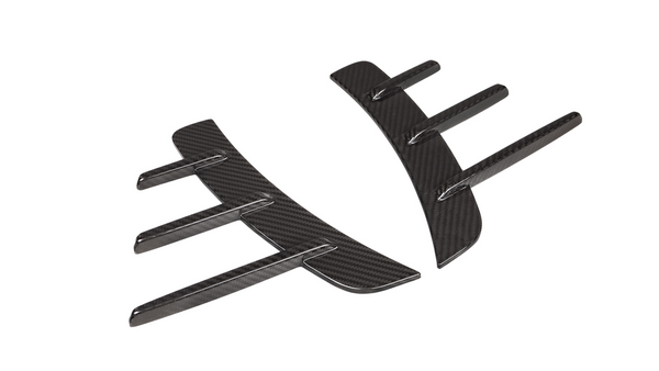 Carbon fiber car parts lie side by side, showcasing aerodynamic fin designs on a white background, highlighting their sleek and modern appearance.