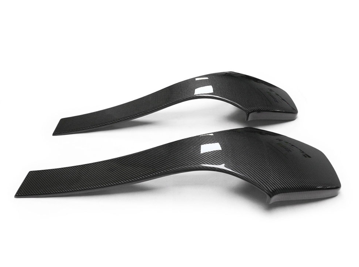Two curved carbon fiber car spoilers rest side by side on a plain white background, exhibiting sleek, aerodynamic shapes with a glossy finish and subtle texture lines.