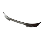 A sleek car spoiler, curved upward at the ends, appears against a plain white background, highlighting its aerodynamic design.