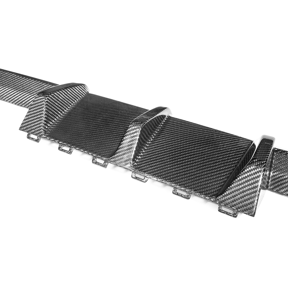 A carbon fiber car diffuser features sleek, angled fins for aerodynamic enhancement, positioned on a flat, metallic surface in a studio-lit environment.