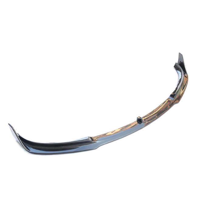 A curved, glossy black car bumper lip lies on a white background, featuring an aerodynamic design with slight ridges, enhancing vehicle aesthetics and performance.