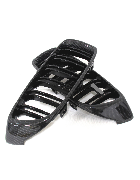 Black car grille covers made of glossy carbon fiber, overlapping each other. They rest on a plain white background, designed for vehicle front-end styling.