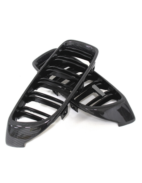 Black car grille covers made of glossy carbon fiber, overlapping each other. They rest on a plain white background, designed for vehicle front-end styling.