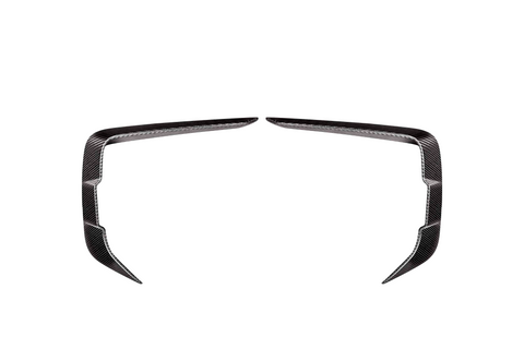 Two symmetrical, angled carbon fiber trim pieces facing each other on a plain white background, resembling elongated, curved brackets or stylized boomerangs.