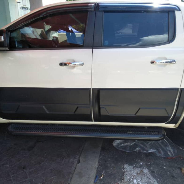 A white pickup truck is parked on a concrete surface, partially visible with its side doors and step board in focus. The background includes a building and other vehicles.