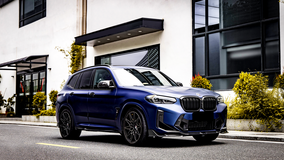 A blue SUV is parked on a street beside a modern white building with large windows and plants, creating a sleek urban setting.
