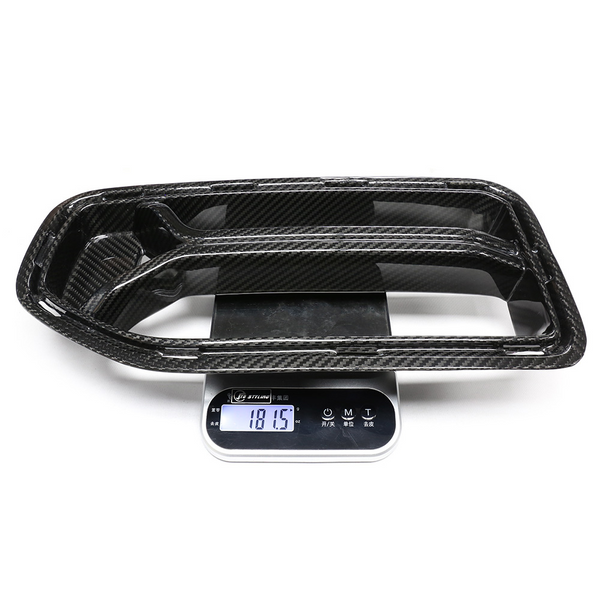 Carbon fiber car part rests on a digital scale displaying "181.5" grams. The scale shows buttons and Asian script, suggesting a precise measurement setting.