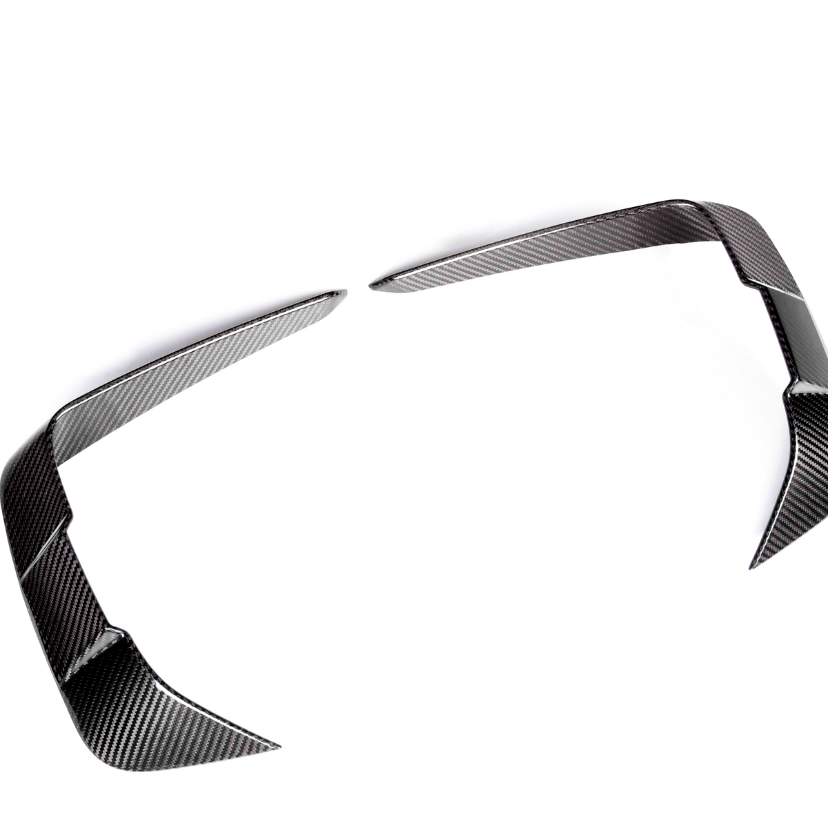 Two carbon fiber trim pieces, angled and sleek, lie on a plain white background, resembling modern automotive design elements, possibly for enhancing vehicle aerodynamics or styling.